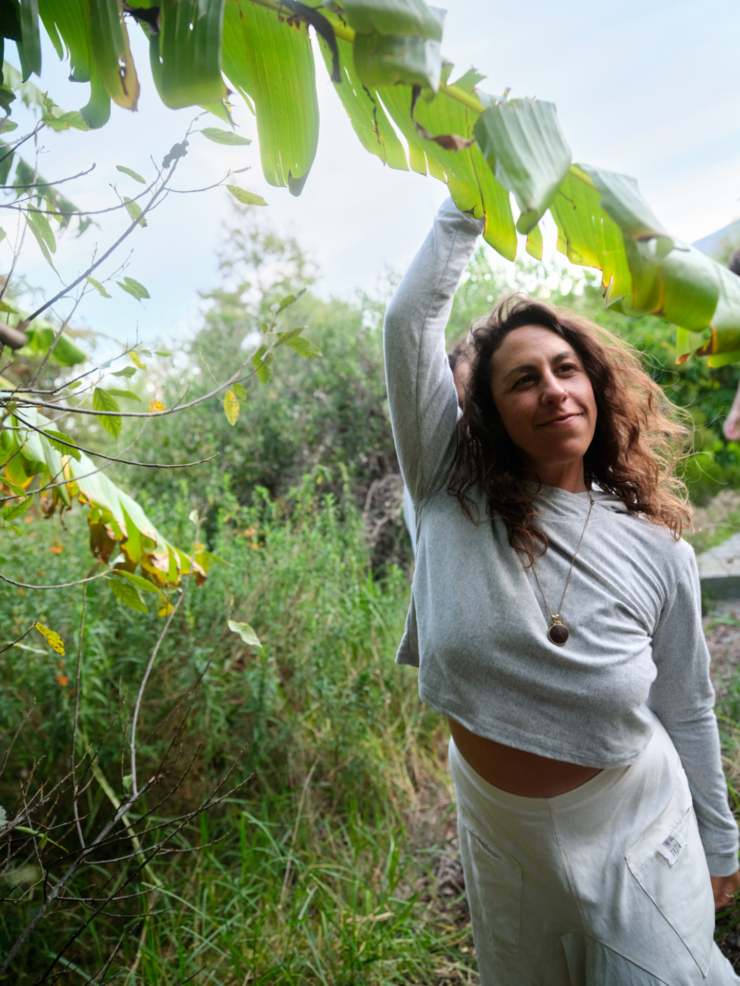 Woman in natural fibres stretching gently beneath banana leaves