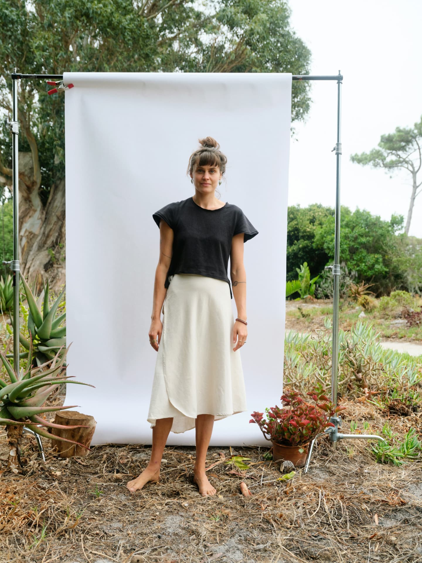 Woman in a black hemp T-shirt and cream skirt against a white backdrop in a garden