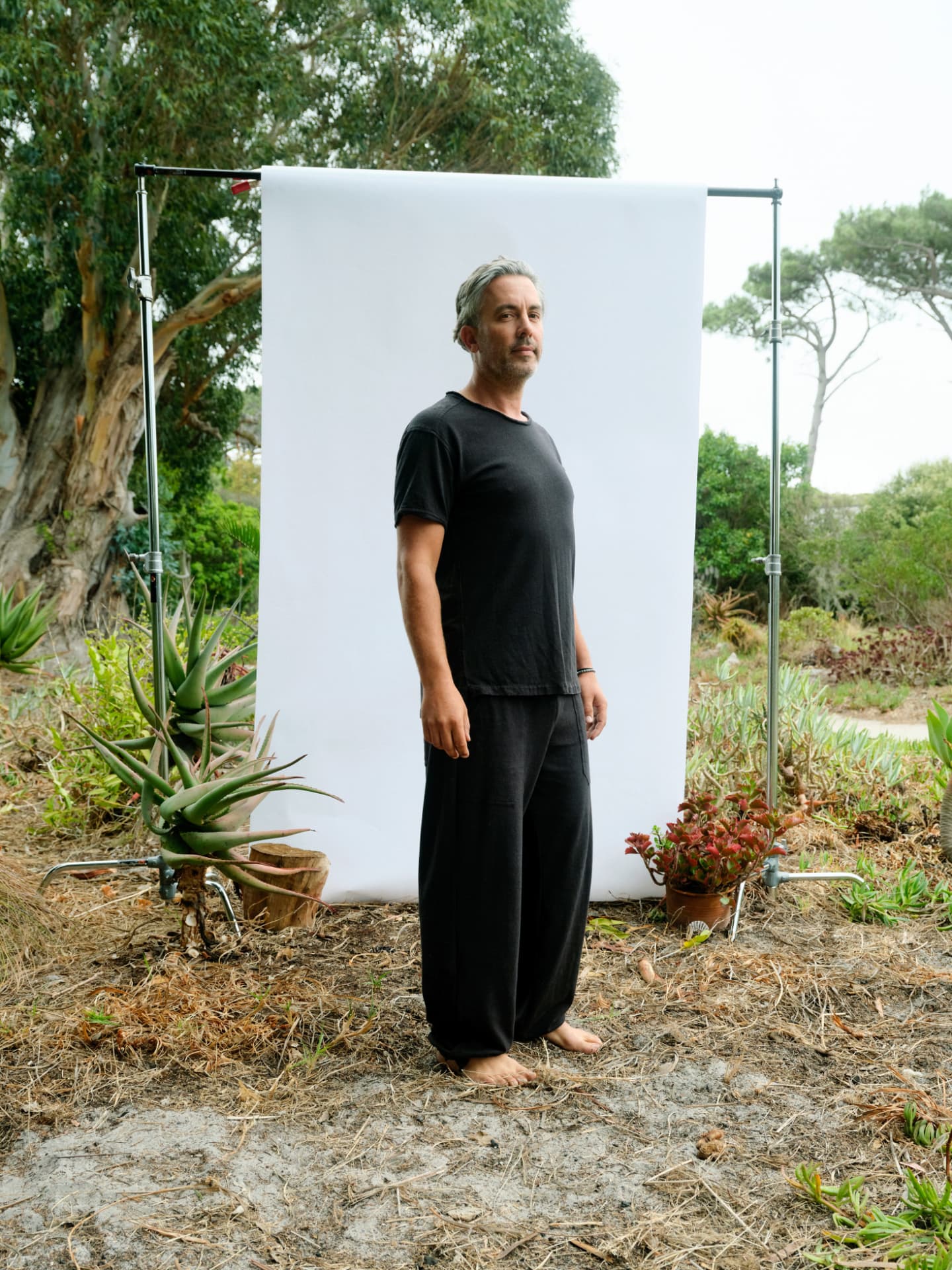 Man in a black hemp T-shirt and loose trousers against a white backdrop in a garden