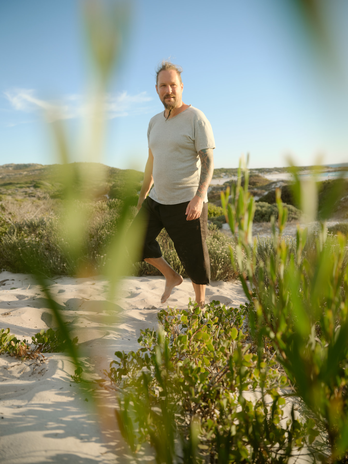 Man in a hemp tee walking barefoot through coastal fynbos